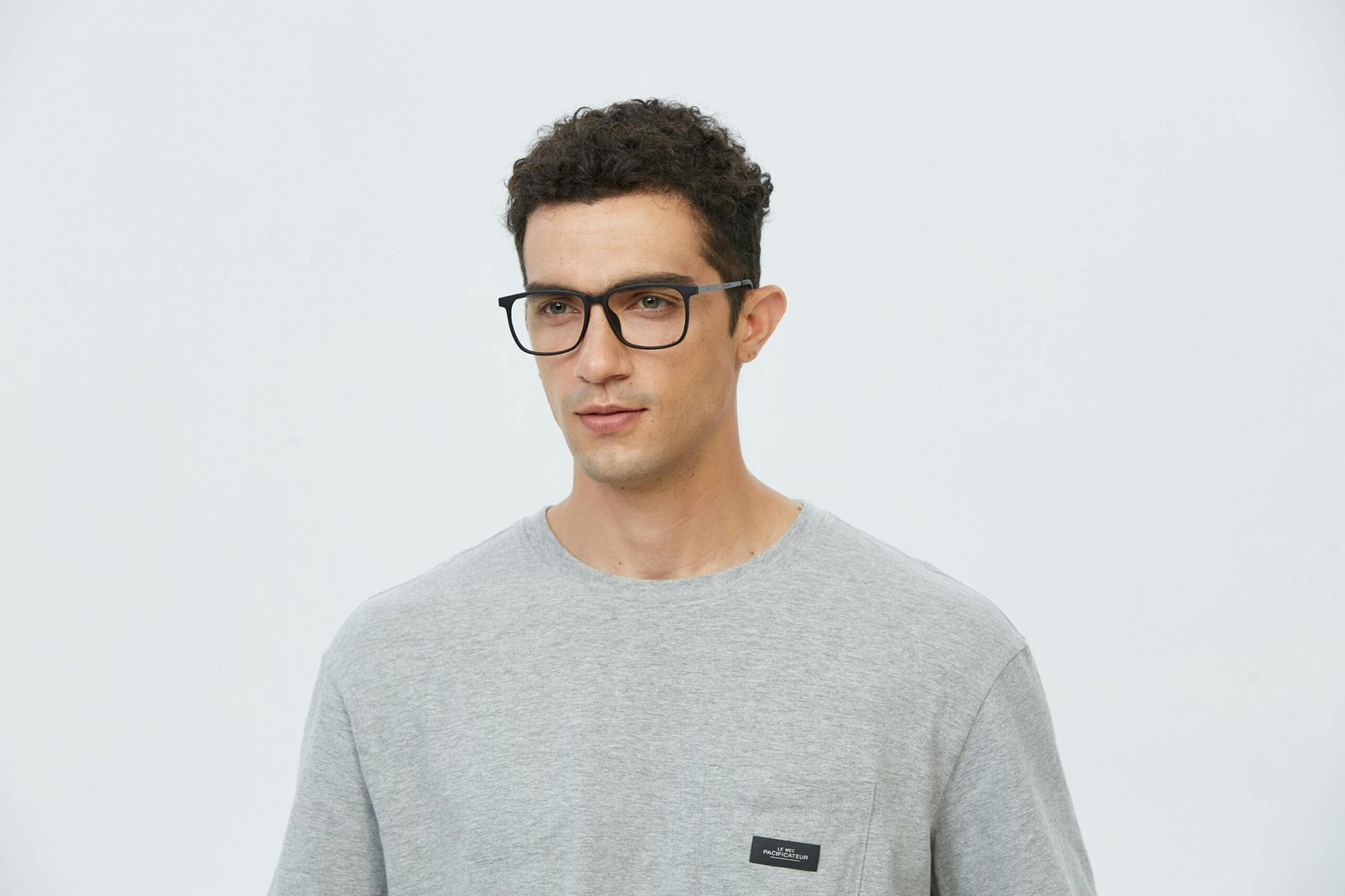 Portrait of a young man wearing glasses in a casual gray t-shirt, looking pensive.